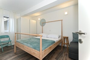 Et moderne soveværelse med en seng med himmelseng i træ, et teal sengetæppe og en grå sofa.