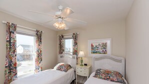 Une chambre avec deux lits, un ventilateur de plafond, une table de chevet avec une lampe et un tableau encadré au mur.