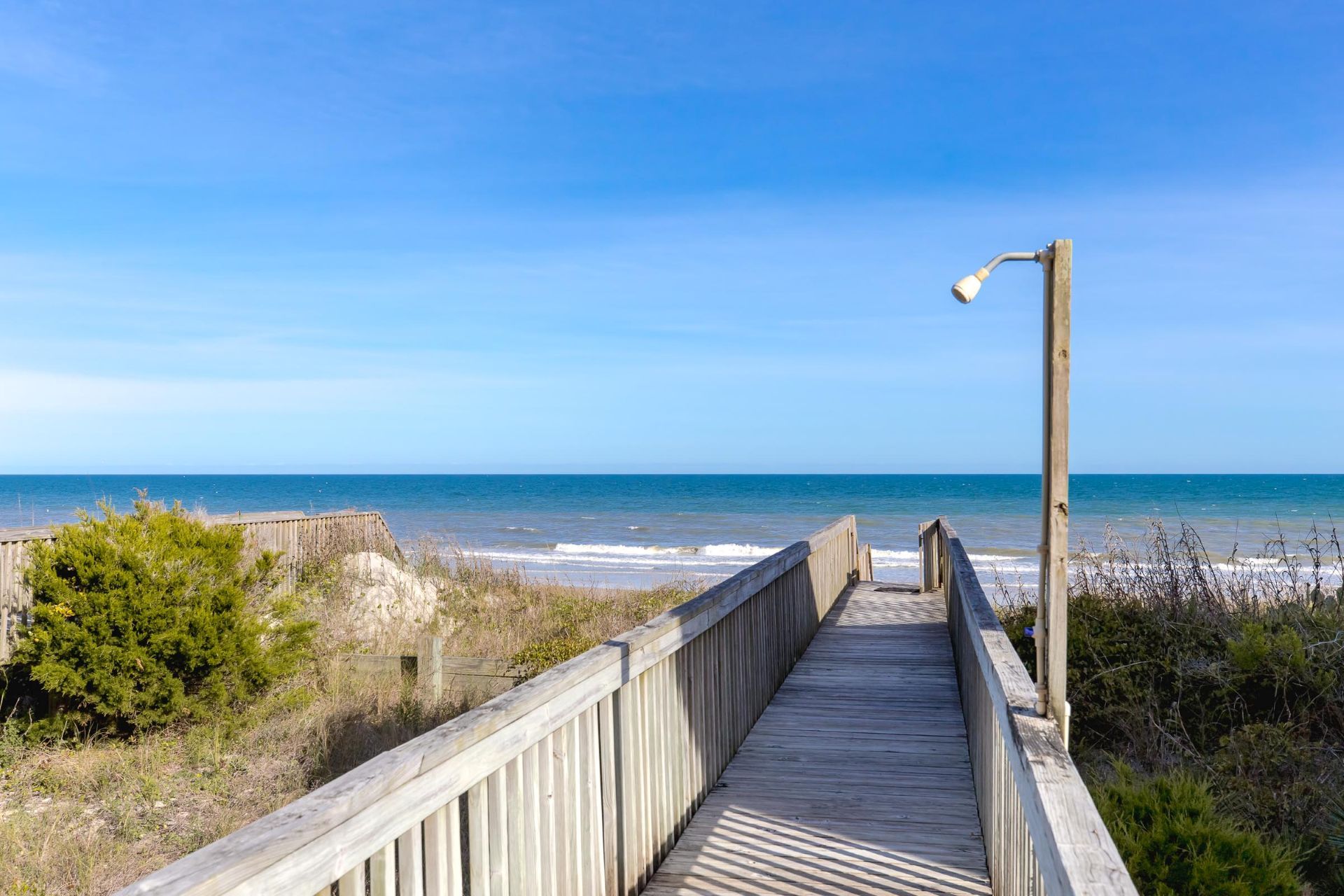 A wooden boardwalk leading to a beach with a clear sky.