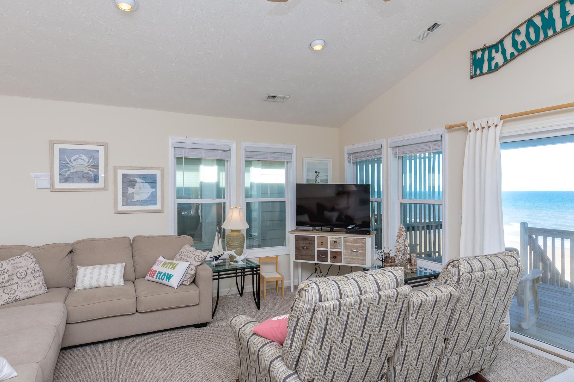 A living room with a sofa, a striped armchair, a TV on a cabinet, and a view of the ocean.