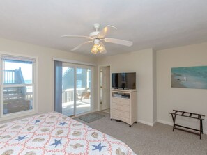 A bedroom with a bed, a ceiling fan, a television on a dresser, and a painting on the wall. - Attitude Adjustment  - 4BR Oceanfront Home; Great Views from the Covered Porches (Surf City)