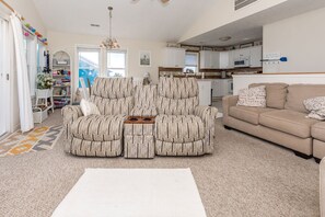A living room with a sofa set, a coffee table, and a kitchen in the background.
