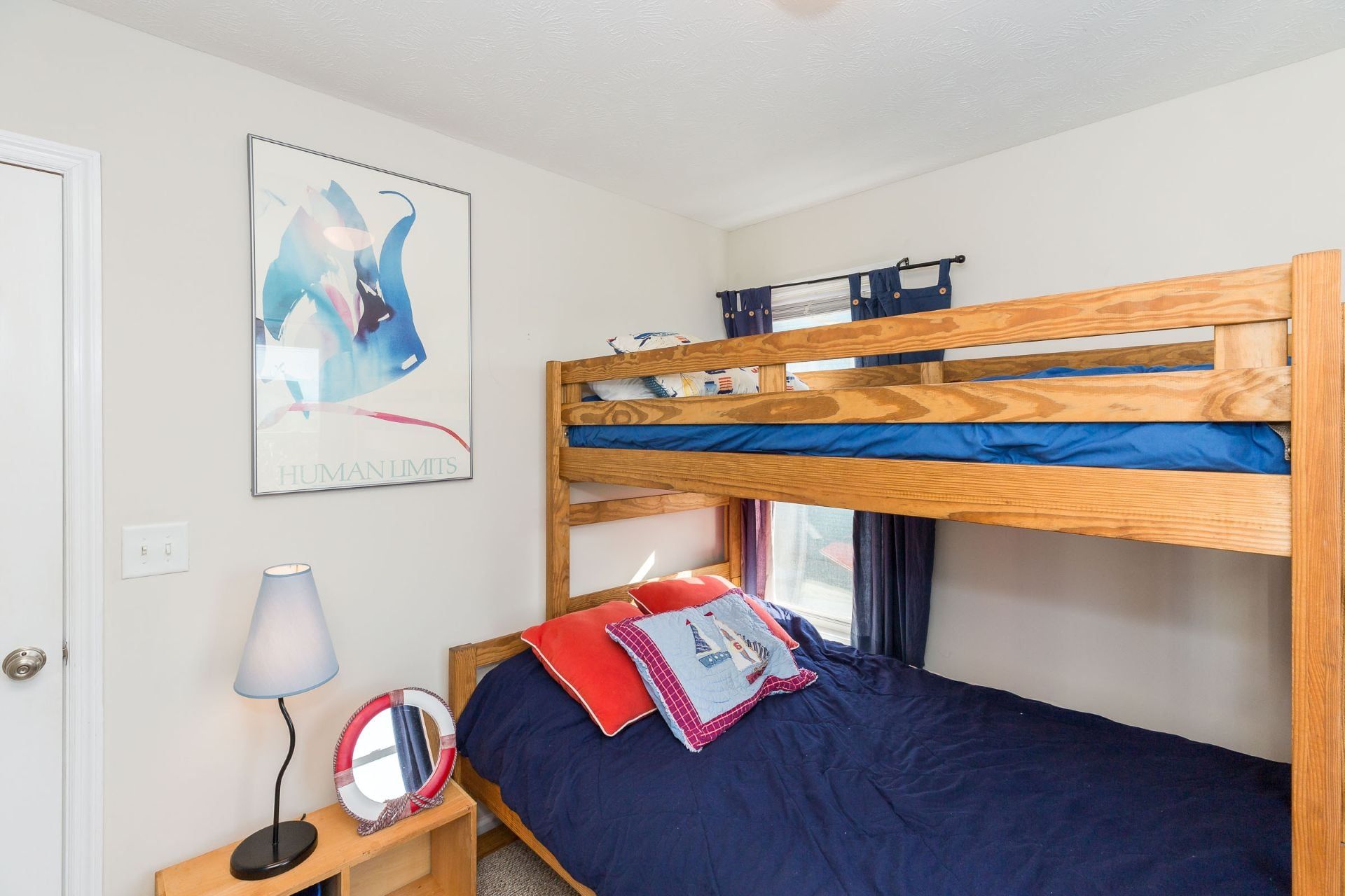 Una cama litera con estructura de madera, una mesita de noche con lámpara, un espejo y un póster en la pared.