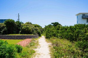 Un sentier de terre serpente à travers un espace paysager, bordé d’une végétation luxuriante et d’un mur de pierres d’un côté.