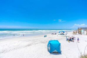 Una playa con cielo despejado, una torre de salvavidas y una carpa azul.