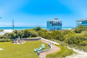 Una propiedad frente al mar con una casa grande, un patio circular con sillas y vista al océano.