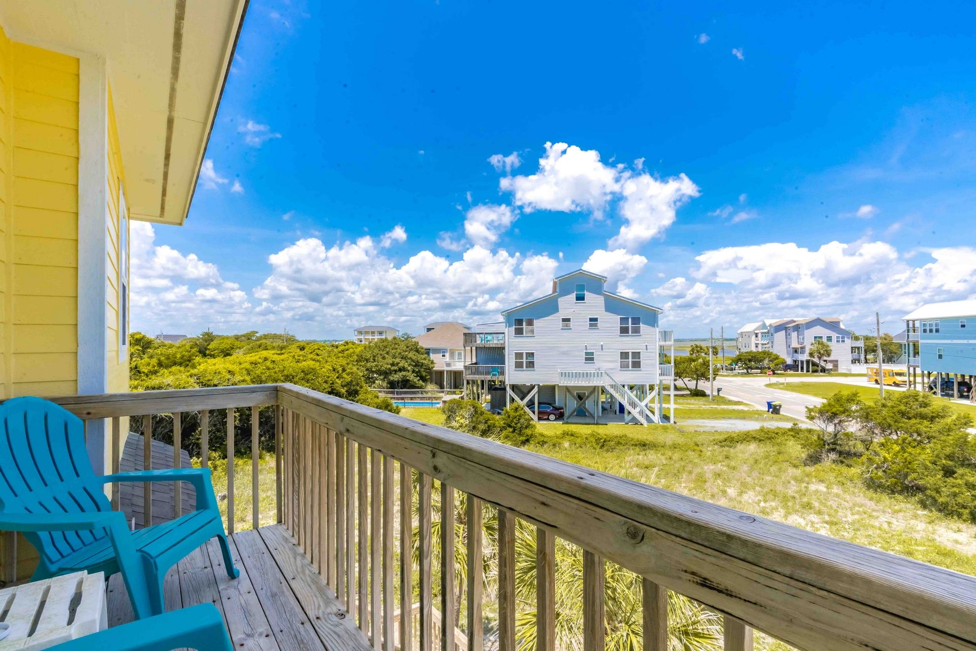 A wooden deck with a blue chair, overlooking a residential area with houses and a clear sky.