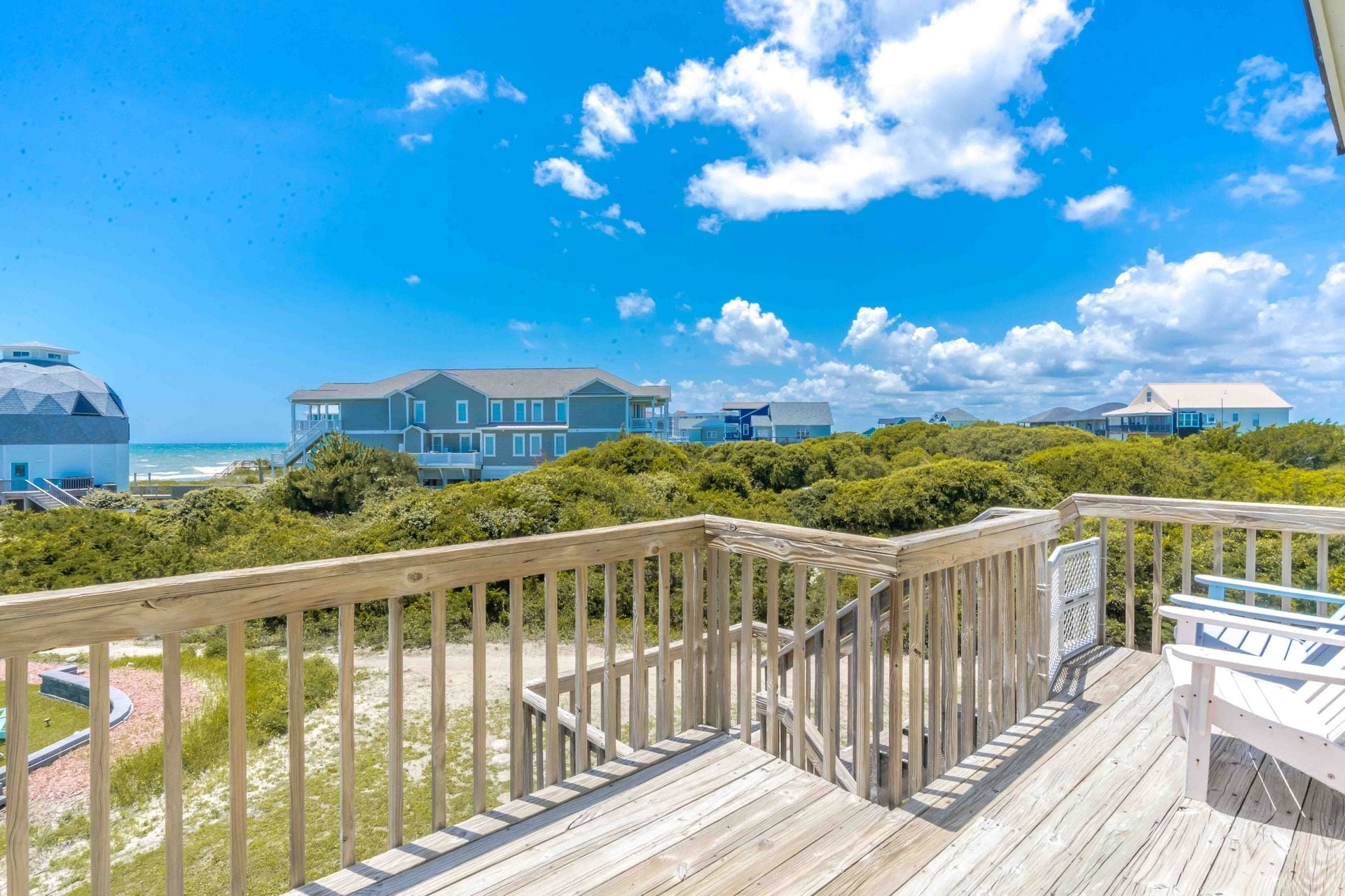 A wooden deck with a view of beachfront houses and ocean.