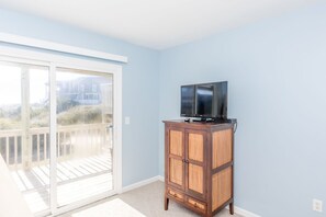 A room with a television on a wooden cabinet, a sliding glass door to a balcony, and a light blue wall.