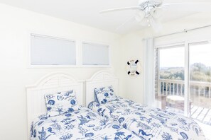 Une chambre à coucher avec un lit, deux fenêtres, un ventilateur de plafond et un balcon avec vue.