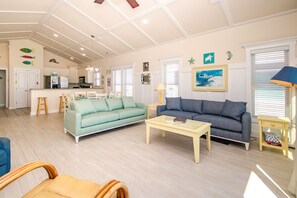 A spacious living area with a sofa, a coffee table, and a dining area with a kitchen in the background. - Topsail Time - Oceanfront 4 BR home in Surf City! Dog Friendly! (Surf City)