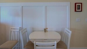 A dining area with a white table and chairs, a small vase on the table, and a framed picture on the wall. - Topsail Time - Oceanfront 4 BR home in Surf City!  Dog Friendly! (Surf City)