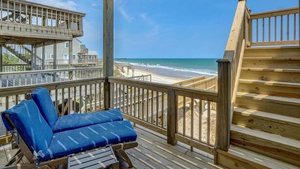 A wooden deck with a blue cushioned lounge chair, a staircase, and a view of the beach. - Topsail Time - Oceanfront 4 BR home in Surf City!  Dog Friendly! (Surf City)