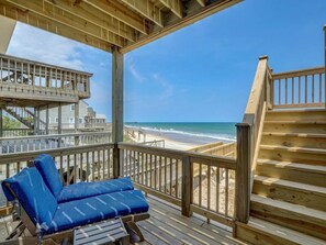 A wooden deck with a blue cushioned lounge chair, a staircase, and a view of the beach.
