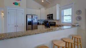 A kitchen with white cabinets, a granite countertop, a refrigerator, a microwave, and a sink. There are three wooden stools at the counter. - Topsail Time - Oceanfront 4 BR home in Surf City!  Dog Friendly! (Surf City)