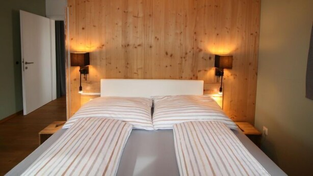 A bedroom with a wooden headboard, two bedside lamps, and a bed with striped bedding. - Apartment Lisa by Interhome (Achensee)