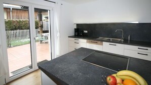 A modern kitchen with a black countertop, a built-in stove, and a sink. There is a sliding glass door leading to a patio with a white fence and greenery. - Apartment Lisa by Interhome (Achensee)