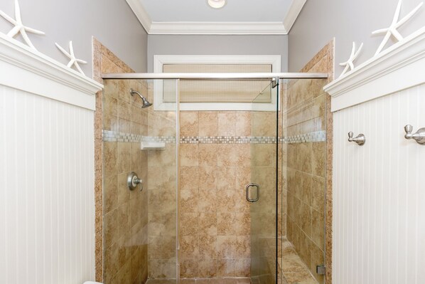 Une douche à l’italienne avec des parois en verre, des carreaux de couleur beige et un pommeau de douche.