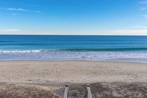 A beach with a wooden fence in the foreground and a clear blue sky.