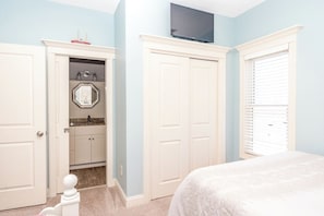 A bedroom with a bed, a TV mounted above a closet, and a bathroom with a sink and mirror. - Dune Time - Spacious 5BR Oceanfront Home - Great Views! (Surf City)
