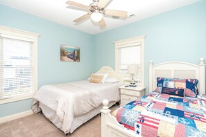 Quarto com cama, mesa de cabeceira, luminária, ventilador de teto e janela com persianas.