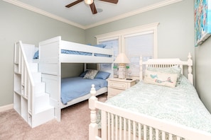 A bunk bed with a desk and chair, a window with blinds, and a ceiling fan.