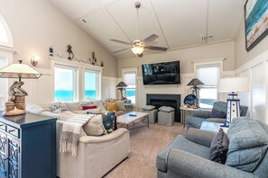 A living room with a fireplace, a ceiling fan, and a television mounted on the wall. - Dune Time - Spacious 5BR Oceanfront Home - Great Views! (Surf City)