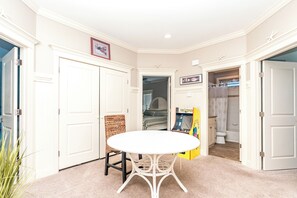 Quarto com mesa e cadeiras brancas, um jogo de Pac-Man e um banheiro com cortina de chuveiro.