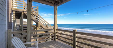 A wooden deck with a view of the ocean, a white chair, and a staircase leading to a covered area.