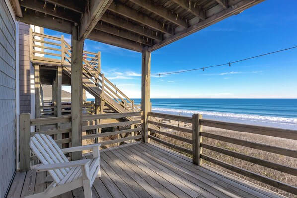 A wooden deck with a view of the ocean, a white chair, and a staircase leading to a covered area.
