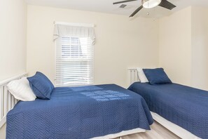 A bedroom with two single beds, white headboards, and a window with blinds. - Que Sea-Ra Sea-Ra - 6BR Oceanfront Home. Private Pool & Hot Tub! Pet Friendly! (North Topsail Beach)