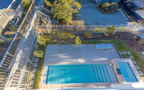 Vue aérienne d’un espace piscine avec une terrasse en bois, un jardin clôturé et un véhicule garé.