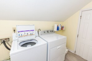 A laundry room with a front-loading washer and dryer, a control panel, and a shelf with cleaning supplies.
