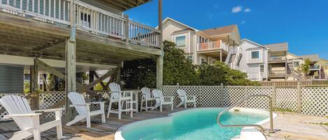 A wooden deck with a pool, white chairs, and a wooden fence.