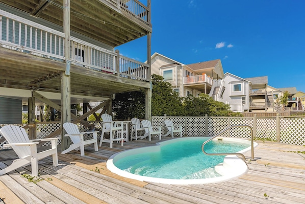 A wooden deck with a pool, white chairs, and a wooden fence.