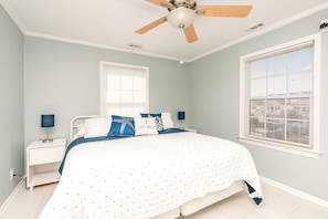 A bedroom with a bed, a nightstand, a lamp, a ceiling fan, and a window.