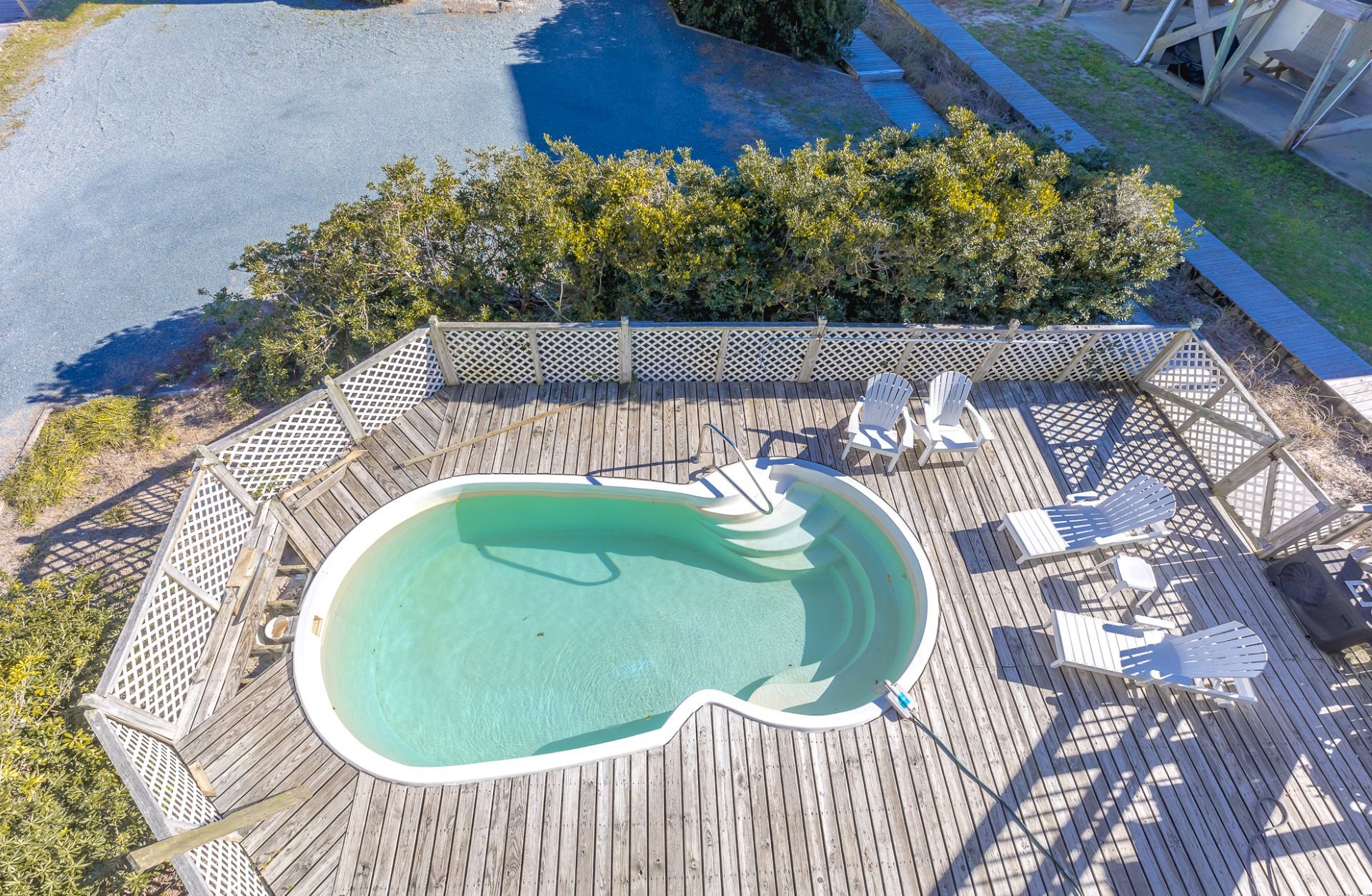 A swimming pool with a wooden deck, surrounded by a fence and chairs.