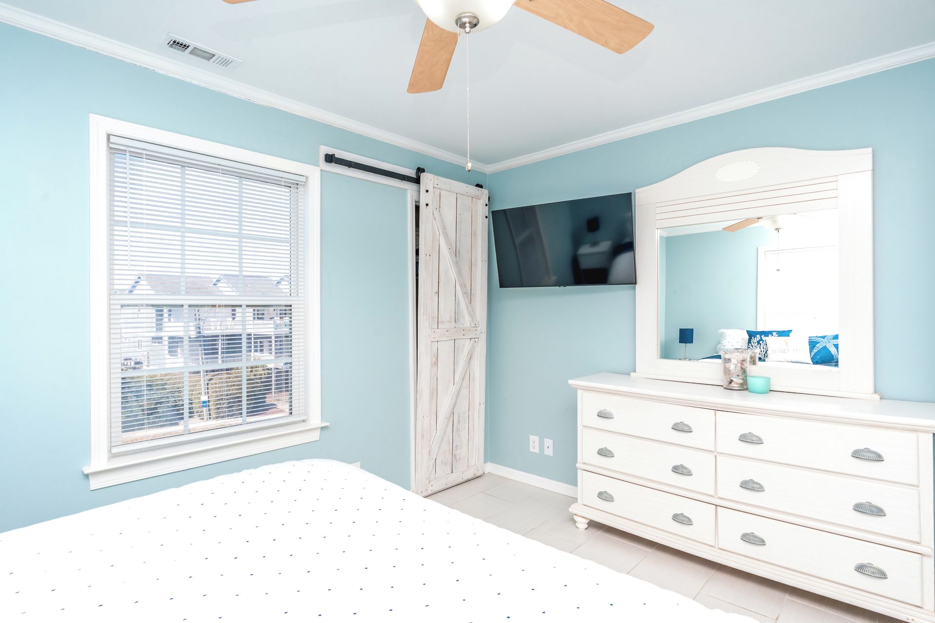 A bedroom with a bed, a dresser, a mirror, a ceiling fan, and a window with blinds.