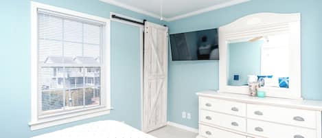 A bedroom with a bed, a dresser, a mirror, a ceiling fan, and a window with blinds.