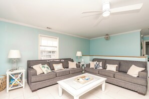A living room with two grey sofas, a white coffee table, and a ceiling fan. - Sea-Sun's Greetings! Steps to the beach! Private Pool!  Pet Friendly! (Surf City)