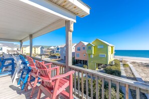 A beachfront property with colorful houses, a covered deck with chairs, and a view of the ocean.