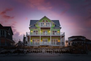 Ein zweistöckiges Strandhaus mit Balkonen, einer umlaufenden Veranda und einem Sandstrand im Vordergrund.