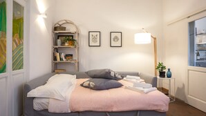 A neatly arranged bedroom with a bed, a bedside table with a lamp, a small shelf with books and a plant, and framed artwork on the wall. - Palazzuolo 118 Cozy apartments (Florence)