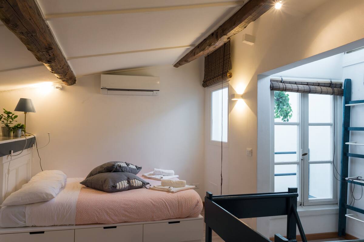 Een slaapkamer met een bed, nachtkastje, lamp, airconditioning en een raam met uitzicht.