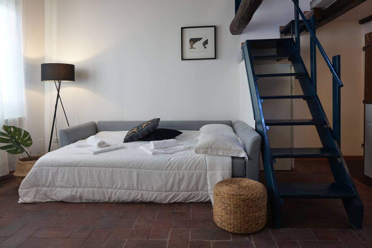 Een slaapkamer met een bed, een vloerlamp, een trap en een ingelijst schilderij aan de muur.