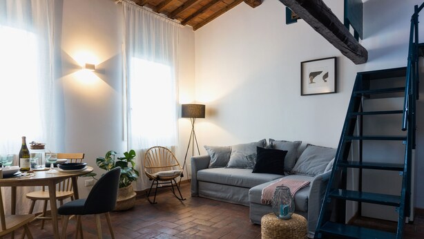 A cozy living room with a sofa, a dining table with chairs, a floor lamp, and a staircase. - Palazzuolo 118 Cozy apartments (Florence)