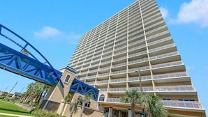 Een hoog hotel met meerdere balkons, een opvallende blauwe brugstructuur en palmbomen op de voorgrond.