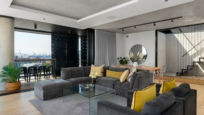 Una sala de estar moderna con un conjunto de sofá, una mesa de centro de vidrio y vistas de la ciudad a través de amplios ventanales.