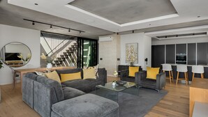 Una sala de estar moderna con un sofá seccional, una mesa de centro de vidrio y un comedor, con una cocina al fondo.