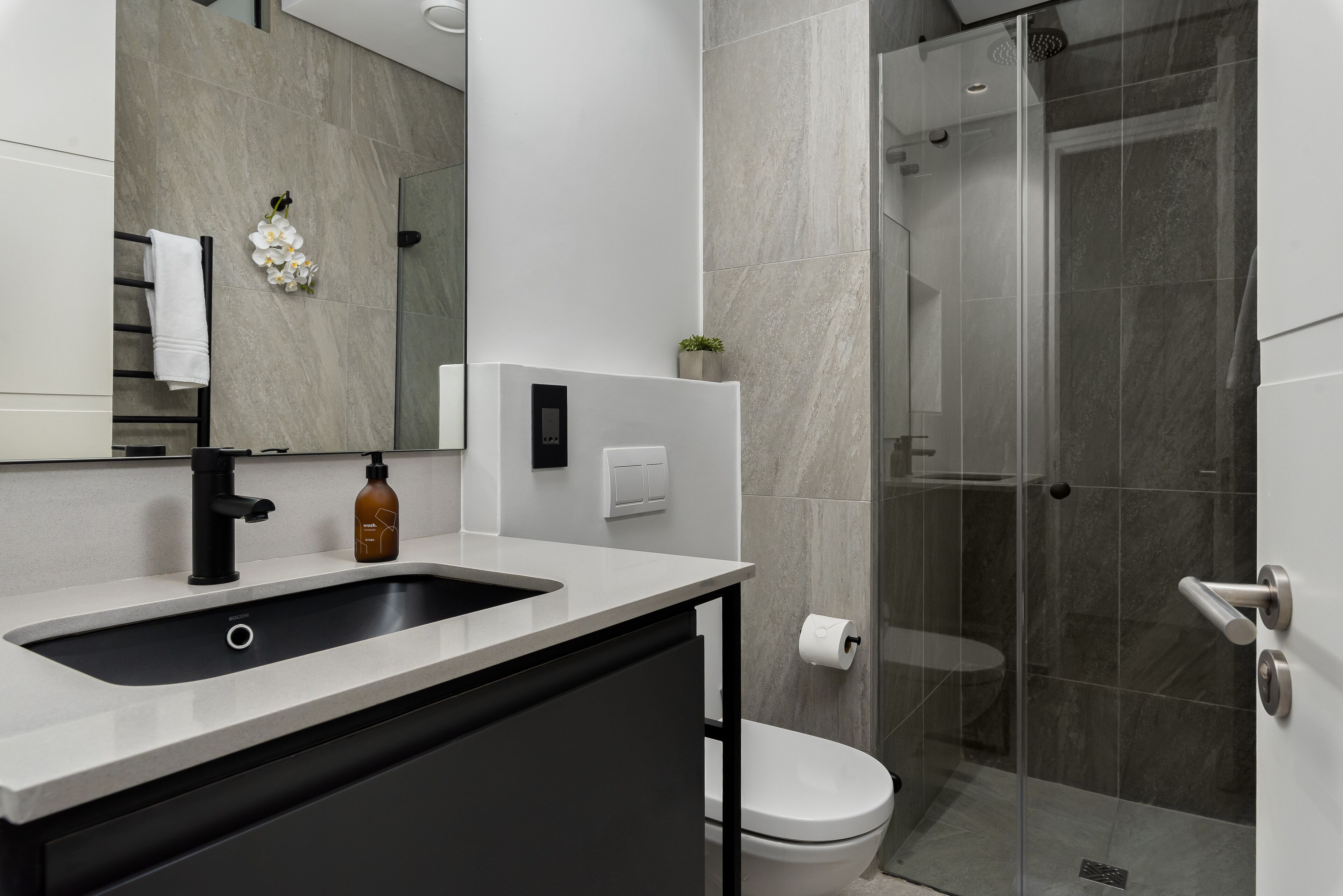 Een moderne badkamer met een grote spiegel, een wastafel, toilet en een douche met glazen wanden.